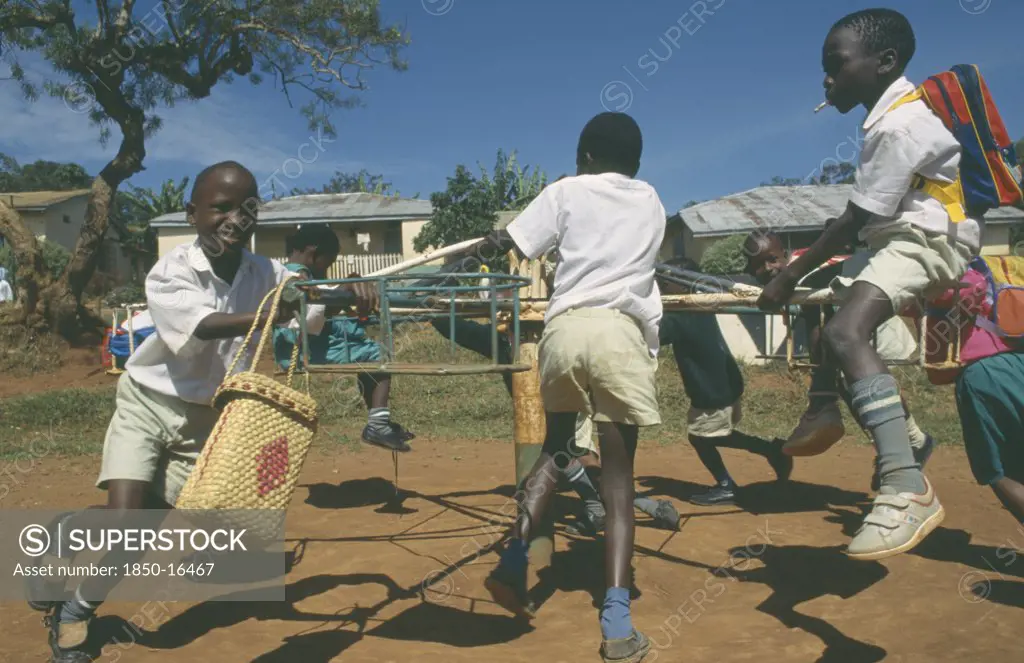 Uganda, Mengo, Primary School Children Playing On Roundabout. Young Boy Smoking Cigarette.