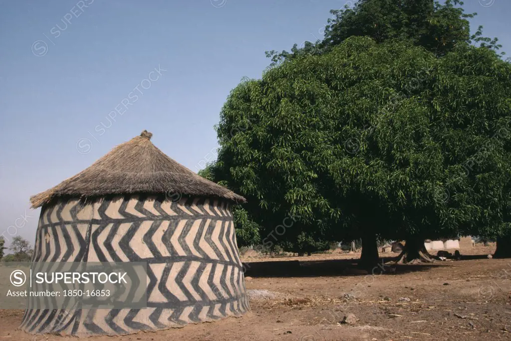 Ghana, Architecture, Traditional Mud Architecture.  Circular Hut Or Granary With Straw Roof And Black And White Abstract Pattern Painted On Wall.