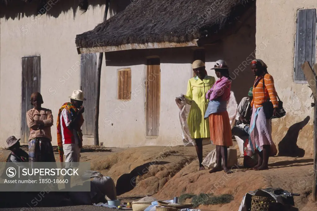 Madagascar, People, Road To Ranomafana. Malagasy Local People Wearing Traditional Colourful Clothing Standing Outside Thatched Housing In A Village