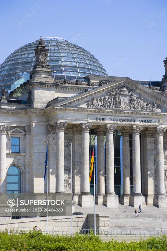 Germany, Berlin, Mitte, The Reichstag building in Tiergarten with the inscrption Dem Deucschen Volke, For the German People, on the facade above the columns at the entrance with Norman Foster's glass roof dome behind.