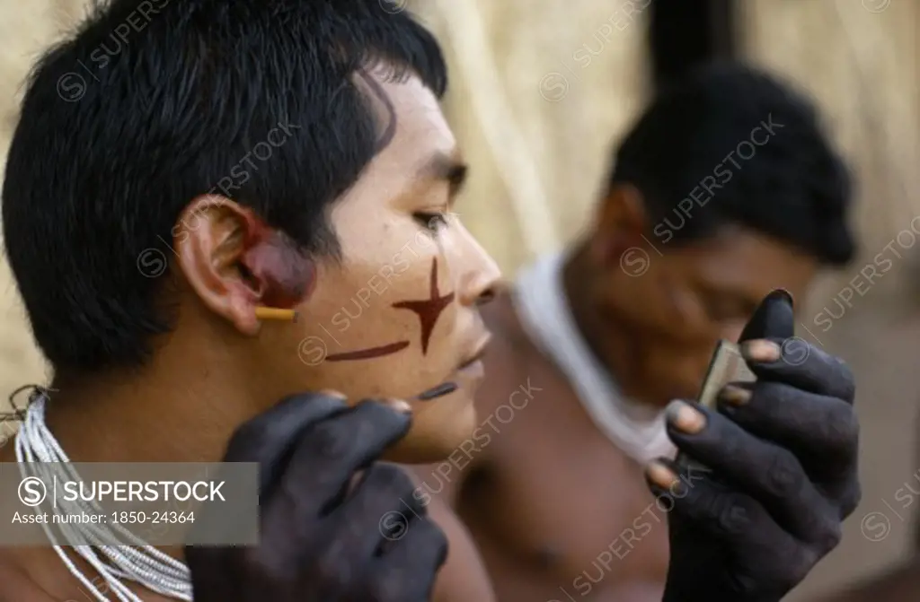 Colombia, North West Amazon, Tukano Indigenous Tribe, 'Barasana Men (Sub Group Of Tukano) Decorating Their Faces With Red Achiote Facial Paint For Ceremonial Dance/Festival Hands, Wrists Blackened With Dark Purple/Black Juice From We Leaves Wearing Necklaces Of Small White Glass Trade Beads '