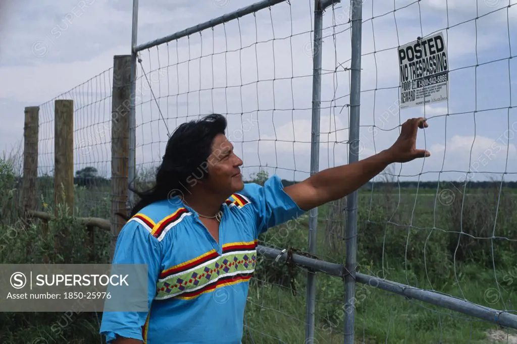 Usa, Florida, Everglades, Independent Seminole Native American Leader Reading A No Trespassing Notice Posted On Fence On Agricultural Land Which Is Actually Indian Land.