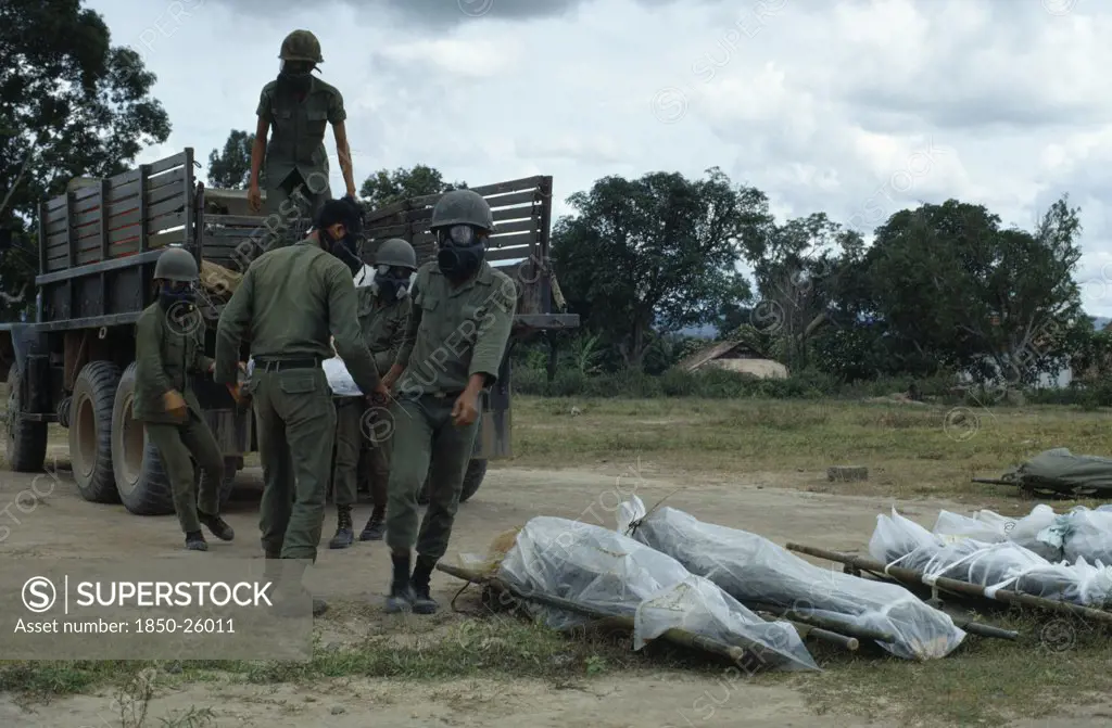 Vietnam, Central Highlands, Kontum, Vietnam War. Siege Of Kontum. Montagnard Soldiers Wearing Gas Masks Unloading Bodies Of Dead In Plastic Body Bags From Truck To Be Shipped Back To Their Village Homes.  Montagnards20092432