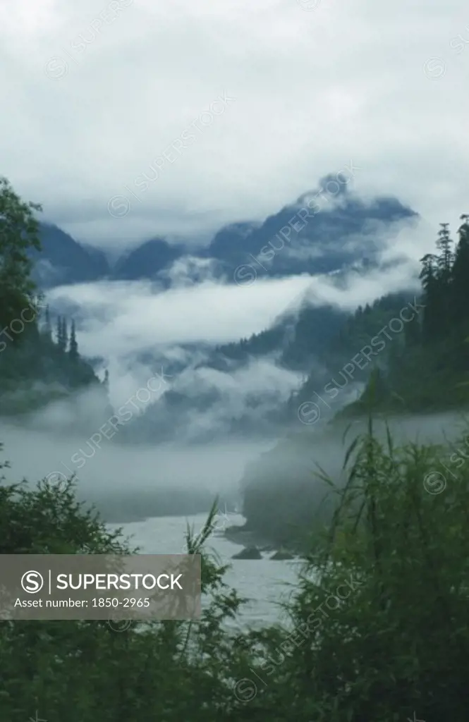 Tibet, Yiang Tsangpo River, Low Clouds In The Tree Lined Valley With Mountains Above