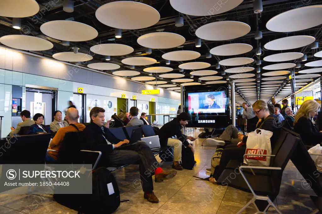 England,  London, Heathrow Airport Terminal 5 disc ceiling in departures zone with passengers waiting in seating area at gate.