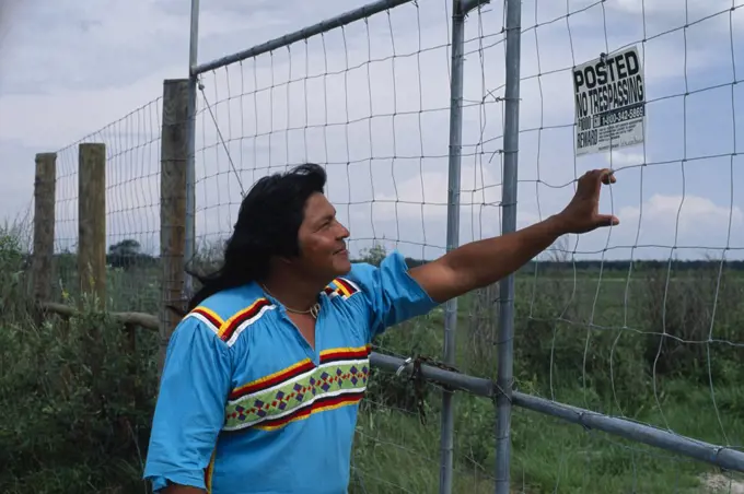 Usa, Florida, Everglades, Independent Seminole Native American Leader Reading A No Trespassing Notice Posted On Fence On Agricultural Land Which Is Actually Indian Land.