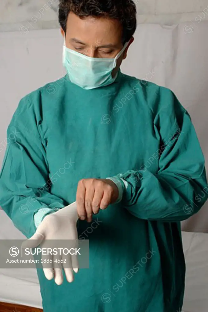 Young Indian Doctor surgeon with face mask, in green operation theatre gown, wearing surgical gloves, in clinic hospital. Model Release Number 637.