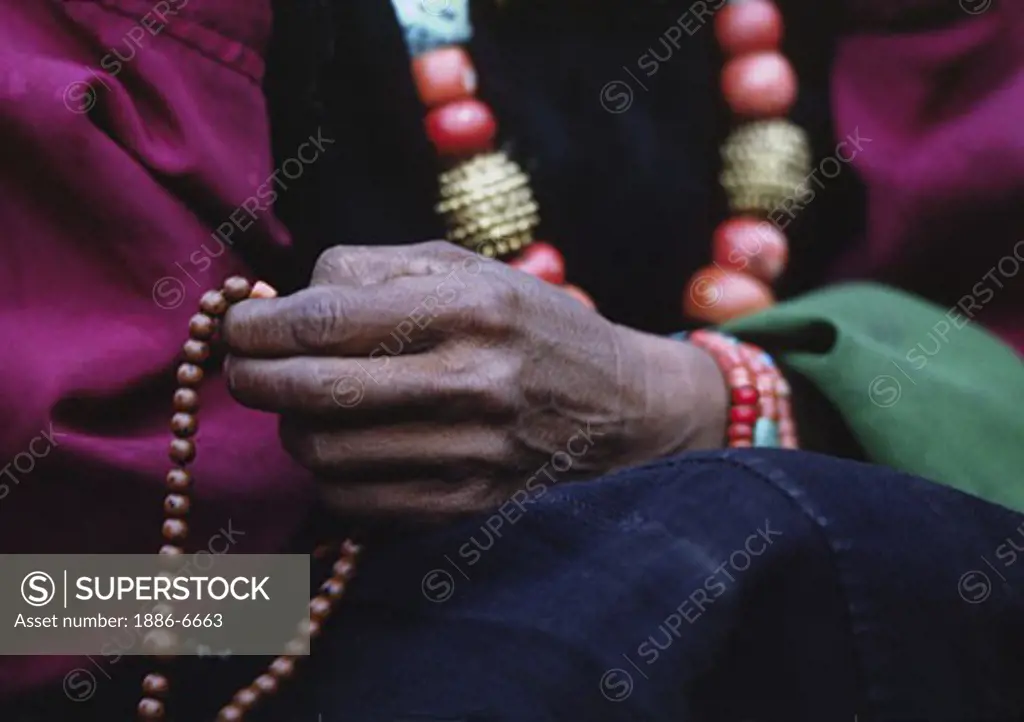 DOLPO WOMAN counts beads on her BUDDHIST ROSARY and wears a CORAL, TURQUOISE and GOLD NECKLACE - DOLPO DISTRICT, NEPAL