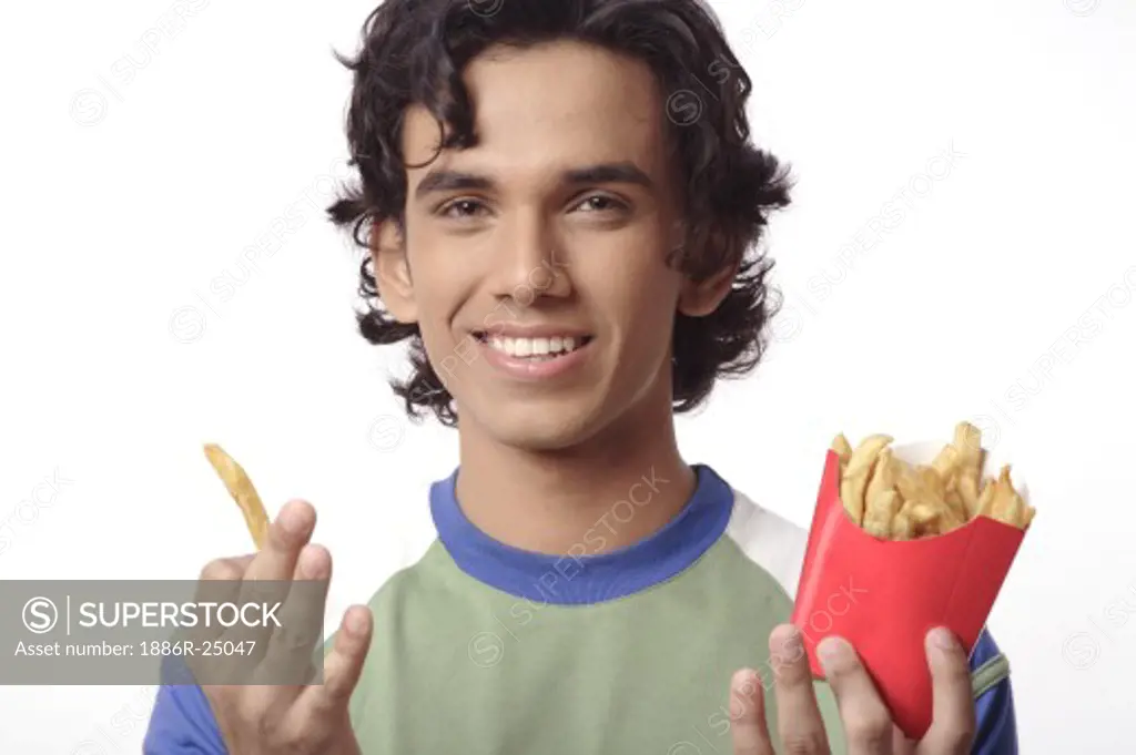 ANG200423 : Teenage boy, standing, holding packet of potato finger chips, French fries, in one hand, one finger chip in hand, smiling, MR #  687T