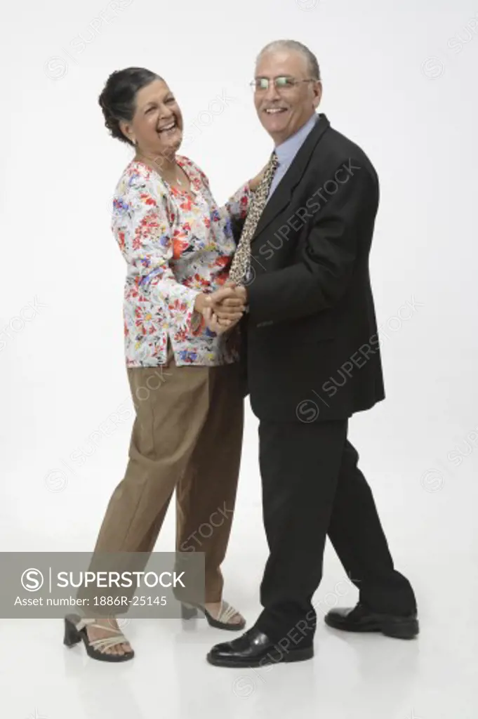 Old couple, senior citizens old man wearing suit, tie, specs, spectacles, glasses, shoes old woman wearing trousers, top with full sleeves and red, blue, yellow gray flowers and leaves, chain with pendent, earrings, sandles old man and woman dancing waltz and smiling, laughing, MR # 703B and 703A