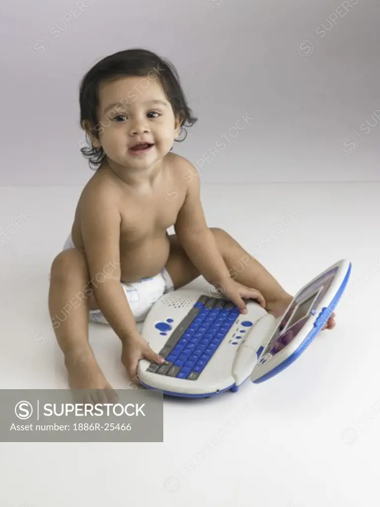 Indian baby girl wearing diaper playing with toy laptop MR#702O