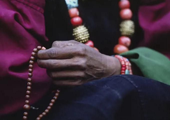 DOLPO WOMAN counts beads on her BUDDHIST ROSARY and wears a CORAL, TURQUOISE and GOLD NECKLACE - DOLPO DISTRICT, NEPAL