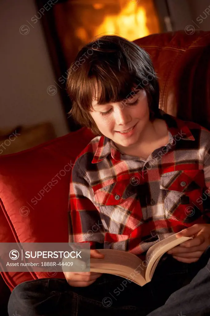 Young Boy Relaxing With Book By Cosy Log Fire