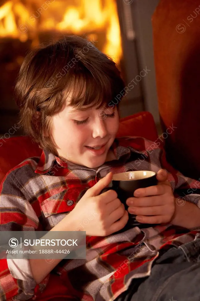 Young Boy Relaxing With Hot Drink By Cosy Log Fire