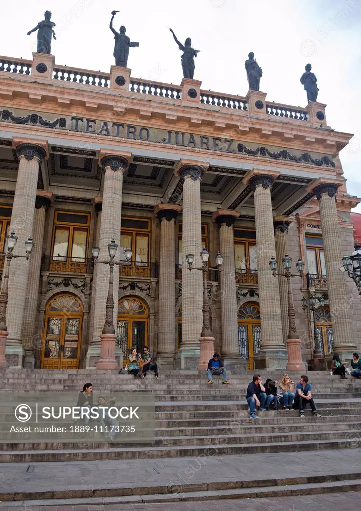 People sitting on the steps of an old spanish theatre with pillars and statues; Guanajuato, Mexico