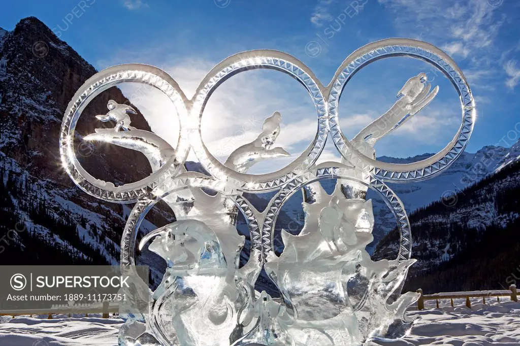 Olympic ring ice sculpture with mountain background, sunburst, blue sky and clouds; Lake Louise, Alberta, Canada