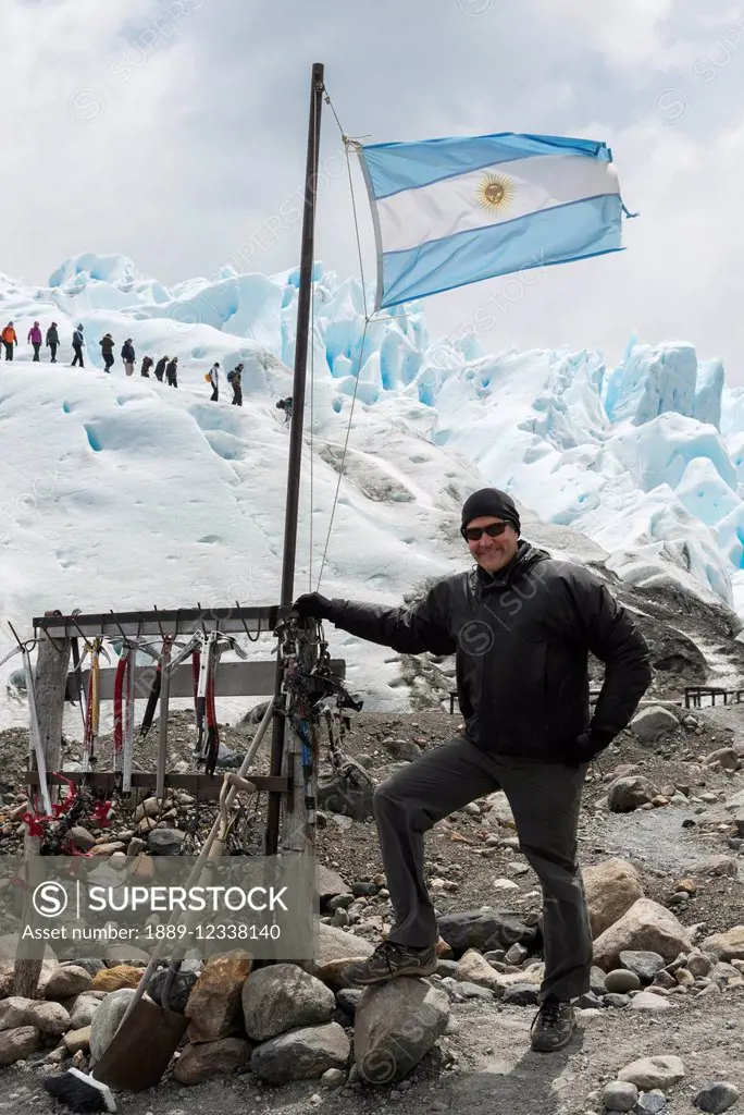 A tourist stands with a flag of Argentina as tourists hike on Moreno Glacier in the background; Santa Cruz Province, Argentina