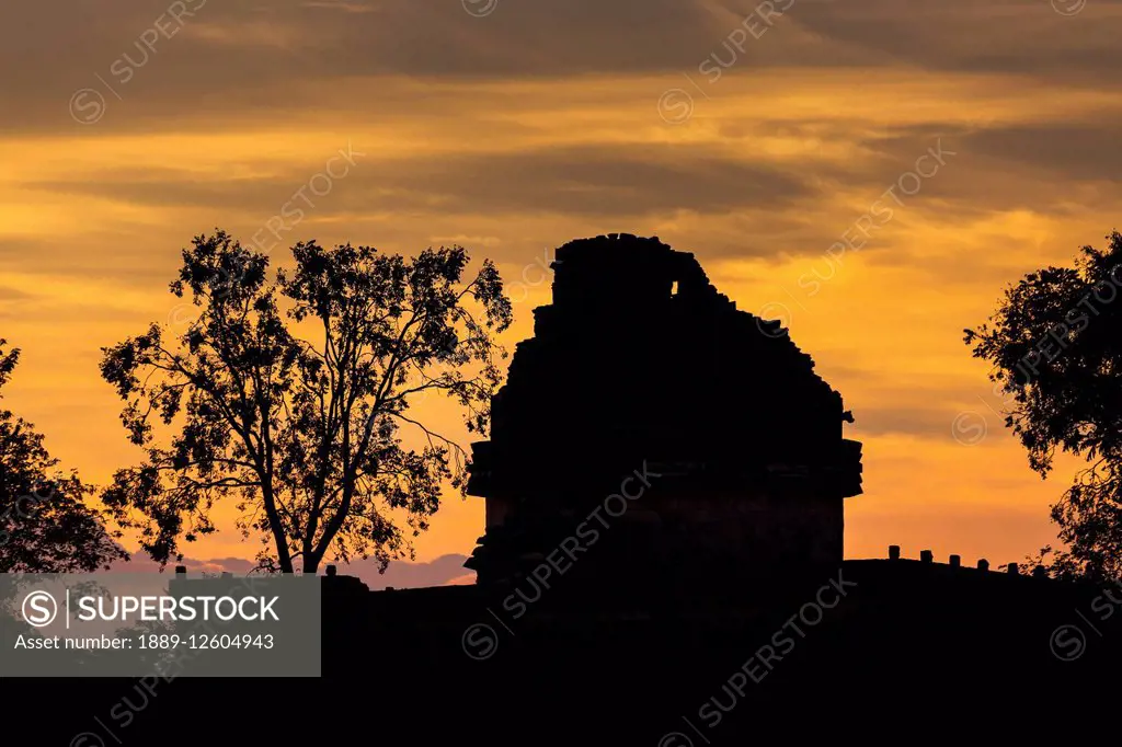 Silhouette of ancient Mayan Observatory with trees and colourful clouds at sunset; Chichen Itza, Yucatan, Mexico