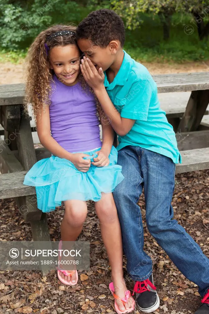 Brother and sister in a park whispering in each other's ears; Menlo Park, California, United States of America