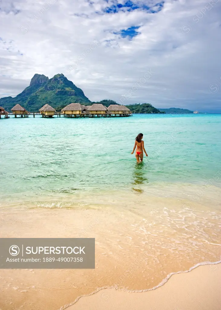 French Polynesia, Tahiti, Bora Bora, Woman In The Ocean With Bungalows In The Background.