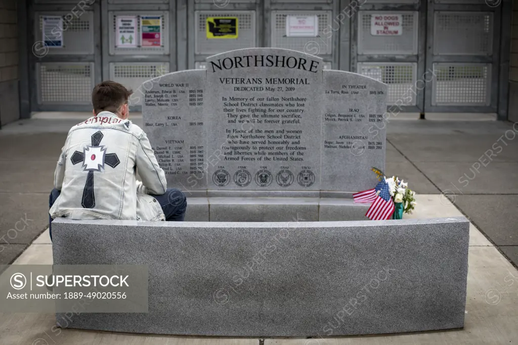 Young man sits in contemplation at an America war veterans memorial; Bothell, Washington, United States of America