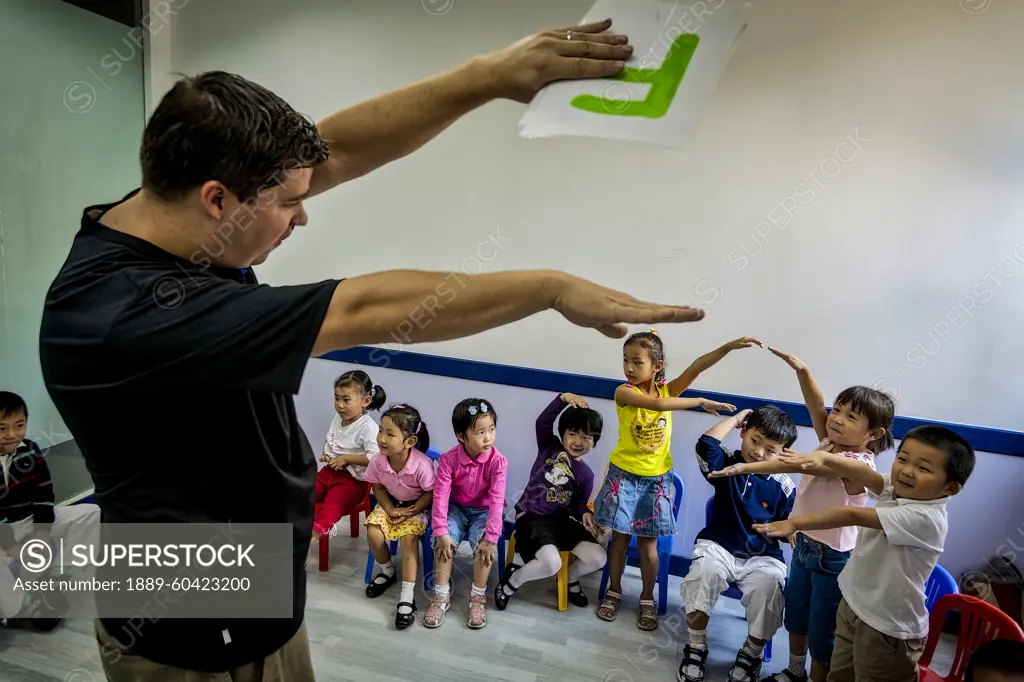 English teacher presents the letter F to preschool children in a classroom. They watch and mimic the gesture; Shanghai, People's Republic of China