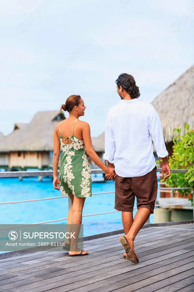 A couple walks along a boardwalk in the bora bora nui resort & spa, bora bora island society islands french polynesia south pacific