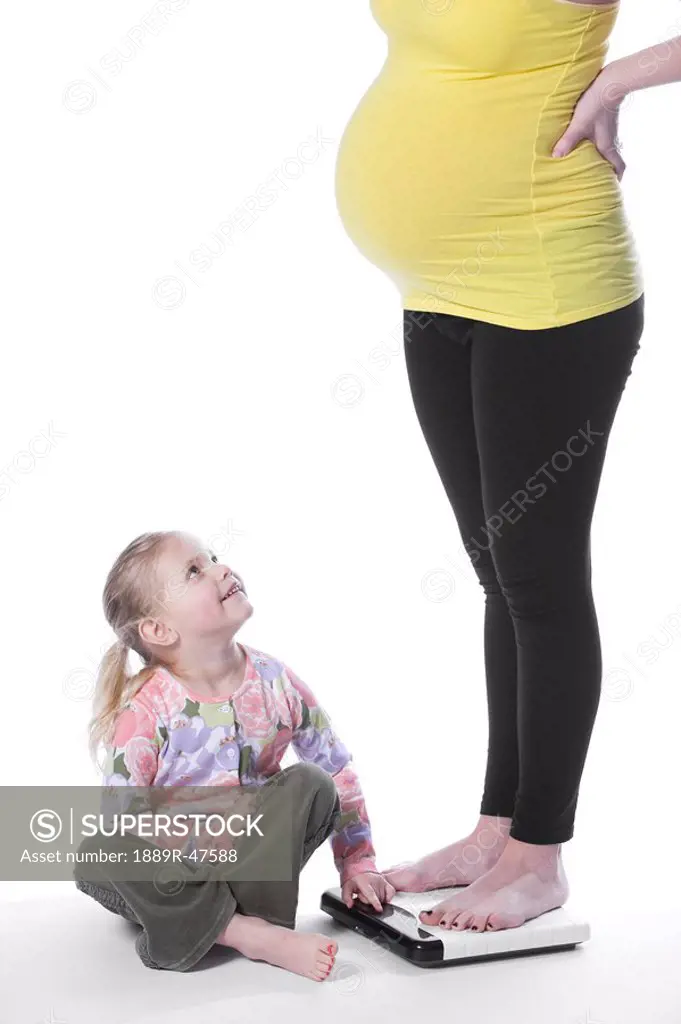 Pregnant mother standing on scale and daughter beside