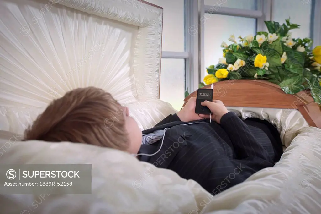 a boy laying in a coffin listening to music