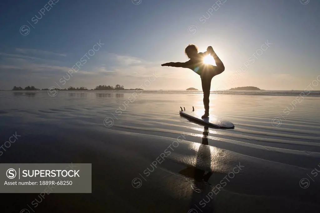 silhouette of female surfer doing bow pulling yoga pose, chesterman beach tofino vancouver island british columbia canada