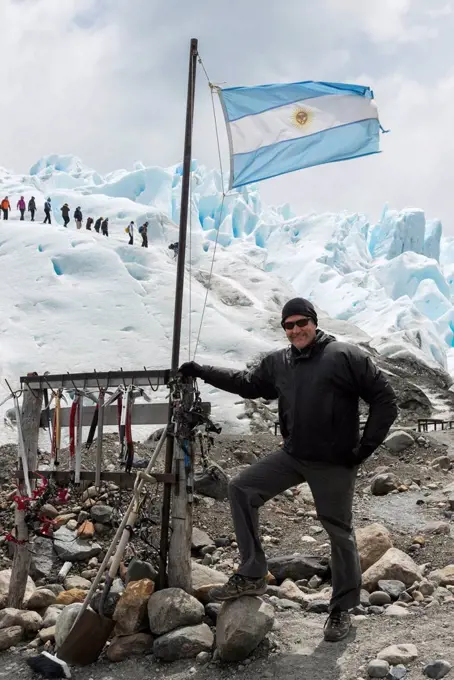 A tourist stands with a flag of Argentina as tourists hike on Moreno Glacier in the background; Santa Cruz Province, Argentina