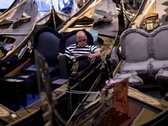 Gondolier reading magazine; Venice, Italy