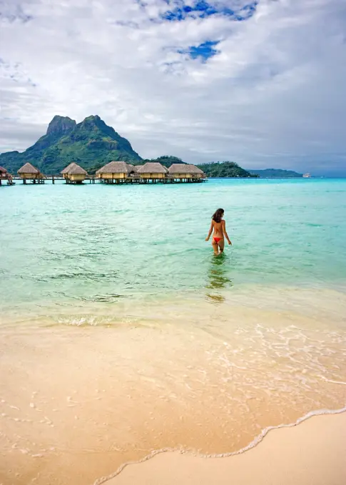 French Polynesia, Tahiti, Bora Bora, Woman In The Ocean With Bungalows In The Background.