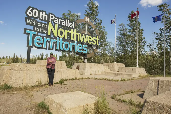 Man Standing Under The Northwest Territories/Alberta Border Sign; Northwest Territories, Canada