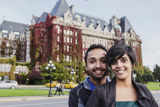 A Young Indian Ethnicity Couple Poses In Front Of The Fairmont Empress Hotel; Victoria, Vancouver Island, British Columbia