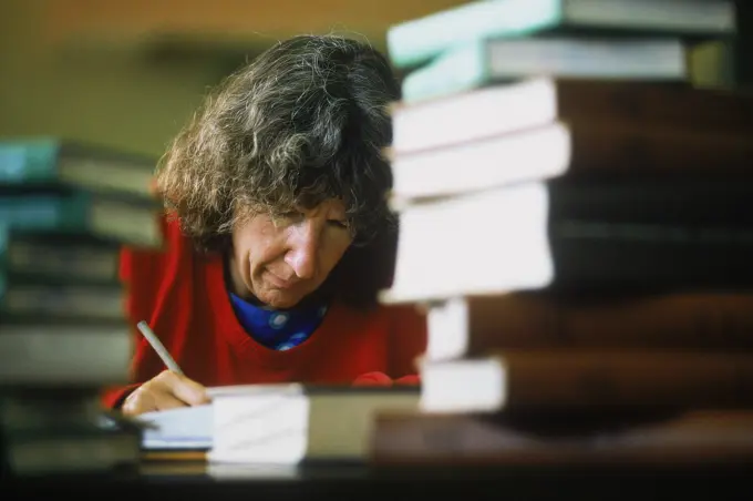 Woman Writing With Stacks Of Books