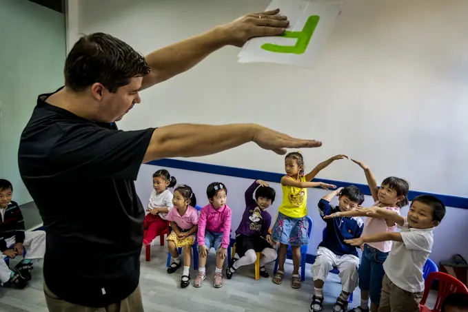 English teacher presents the letter F to preschool children in a classroom. They watch and mimic the gesture; Shanghai, People's Republic of China