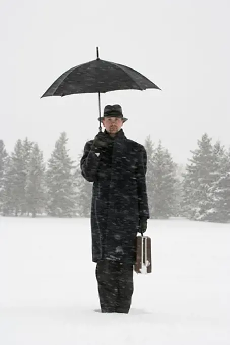 Businessman waiting in the snow with umbrella and briefcase