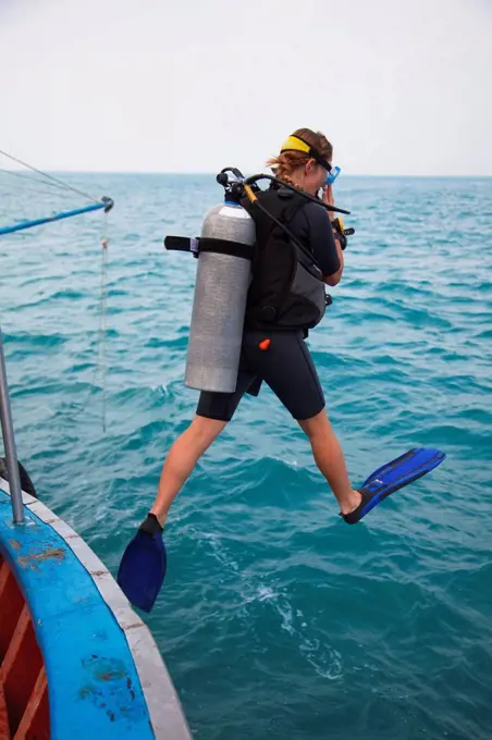 female scuba diver jumps in water, koh tao, thailand