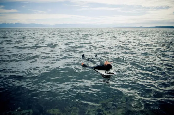 A surfer lays on his back on his surfboard in the water, victoria british columbia canada