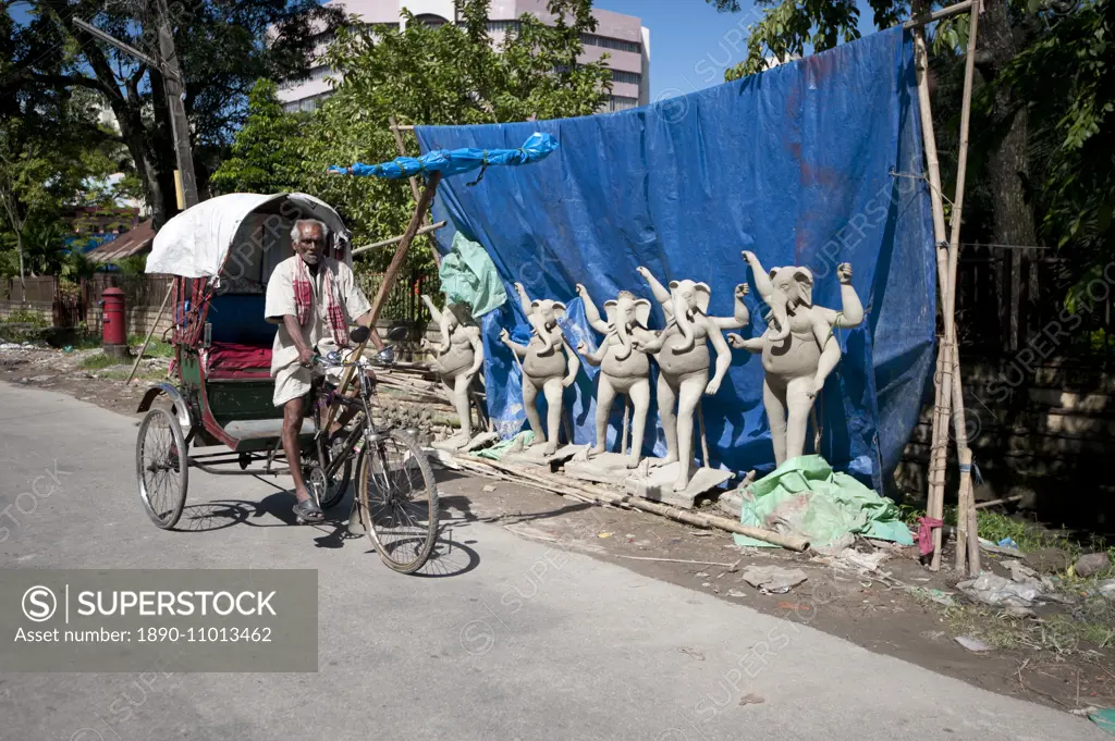 Cycle rickshaw passing row of Ganesh deities made from mud from the Brahmaputra River in preparation for Durga puja celebrations, Guwahati, Assam, Ind...