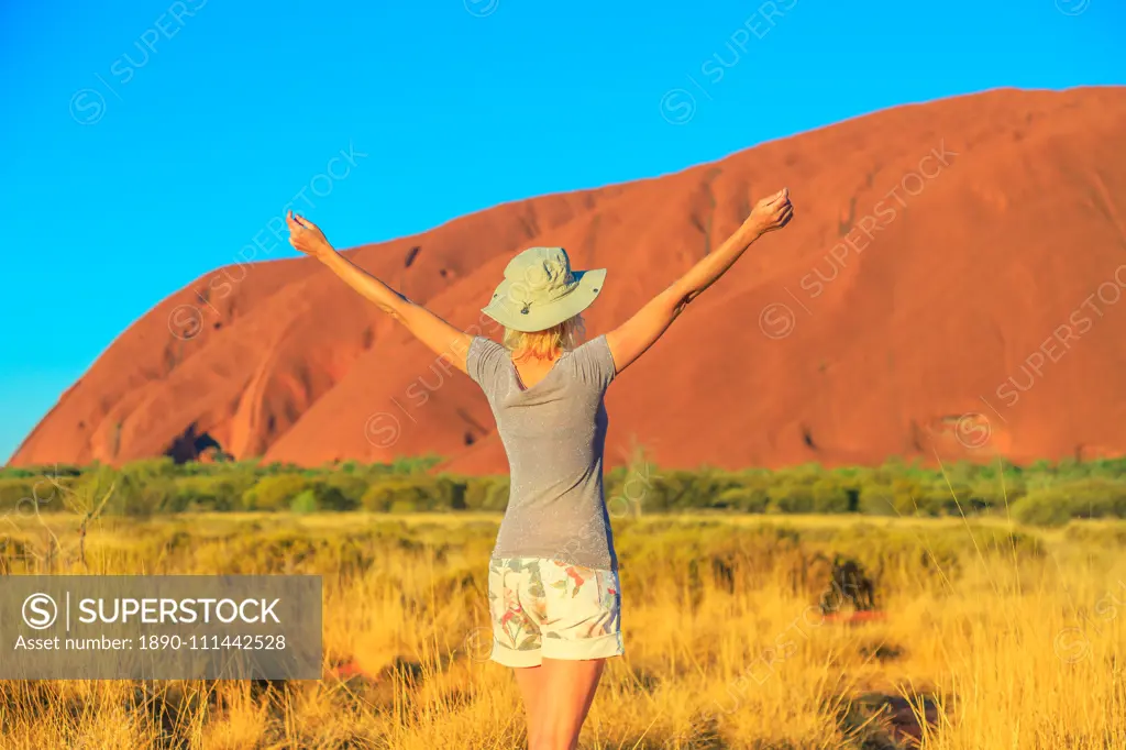 Carefree tourist woman with raised arms enjoys Uluru (Ayers Rock) at sunset in Uluru-Kata Tjuta National Park, UNESCO World Heritage Site, Northern Territory, Australia, Pacific