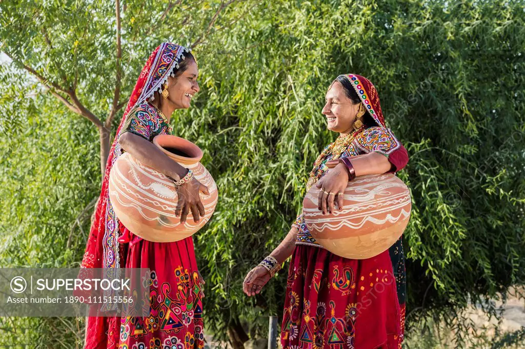 Two Ahir Women in traditional colorful clothes carrying water in a clay jug, Great Rann of Kutch Desert, Gujarat, India, Asia