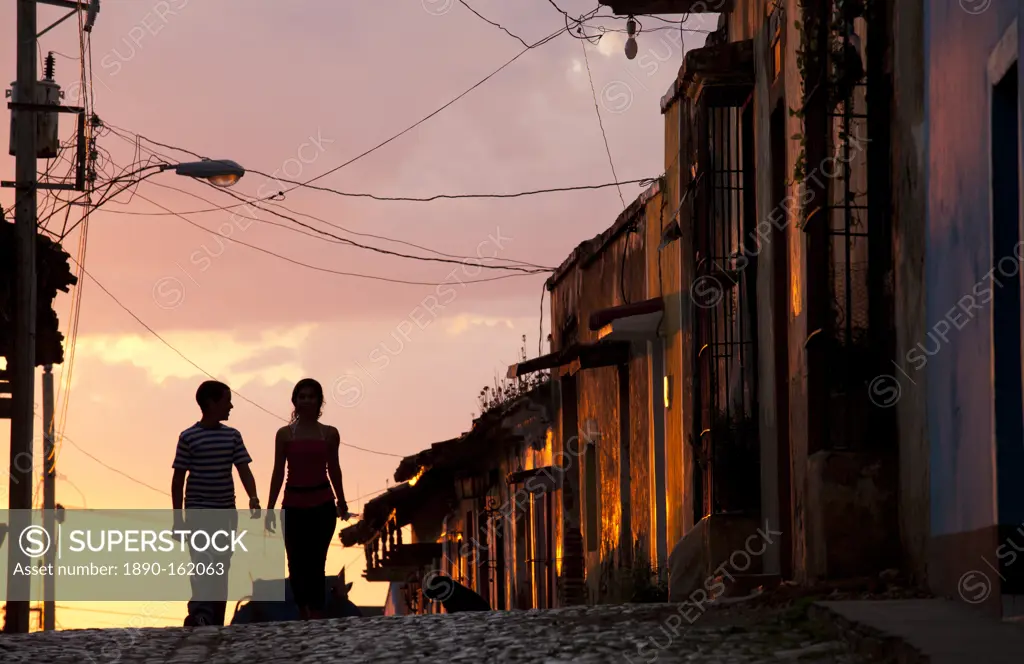 Two young people in silhouette at sunset on cobbled street with colourful orange sky behind, Trinidad, UNESCO World Heritage Site, Cuba, West Indies, ...