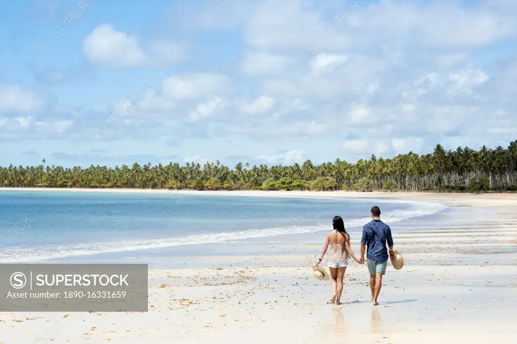 A good-looking Hispanic (Latin) couple walking on a deserted beach with backs to camera, Brazil, South America