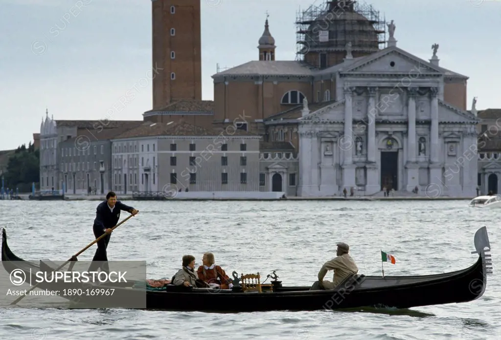 Tourists taking gondola ride propelled by gondolier along canal in Venice, Italy