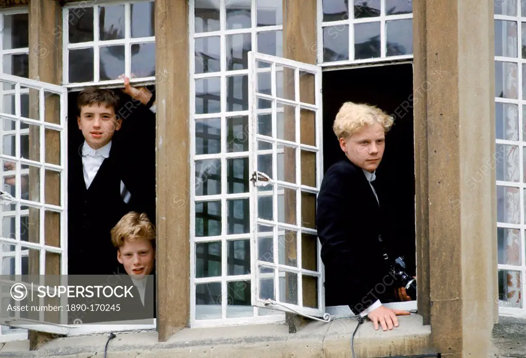 Eton schoolboys in traditional tails looking through the window at Eton College, England, UK