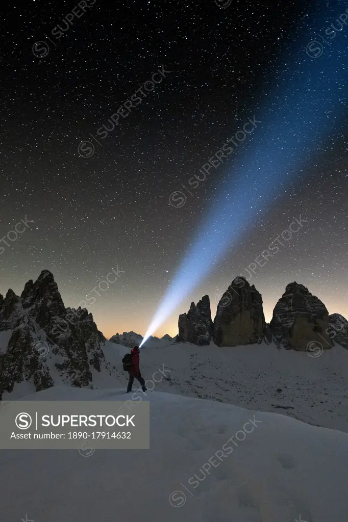 Hiker with head torch admiring stars on Monte Paterno and Tre Cime di Lavaredo, Sesto Dolomites, South Tyrol, Italy, Europe