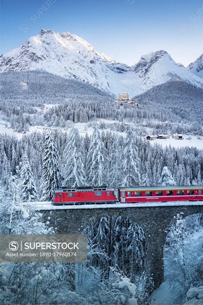 Bernina Express train in the winter forest covered with snow surrounding Tarasp Castle, Engadine, Graubunden Canton, Switzerland,  Europe