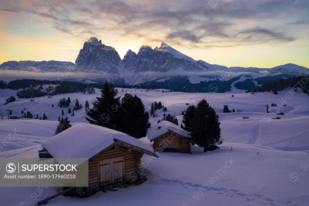 Wood cabins covered with snow with Sassopiatto and Sassolungo in background at dawn, Seiser Alm, Dolomites, South Tyrol, Italy, Europe